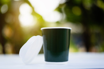A paper cup of hot coffee with smoke at sunrise