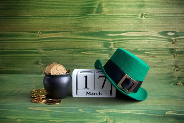white block calendar for St Patrick's Day, March 17, with Leprechaun hat and pot of gold, on green wooden background.