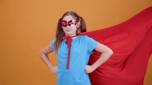 Girl playing the role of a superhero from the movie. Orange Background and slow motion of wind blowing the cloak.