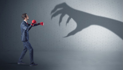 Tiny businessman fighting with scary hand shadow
