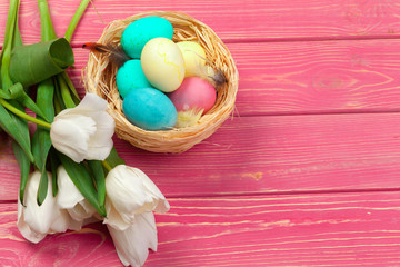 easter, holidays, tradition and object concept - close up of colored eggs and tulip flowers over wooden boards background