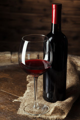 Bottle and glass of red wine on wooden barrel shot with dark wooden background
