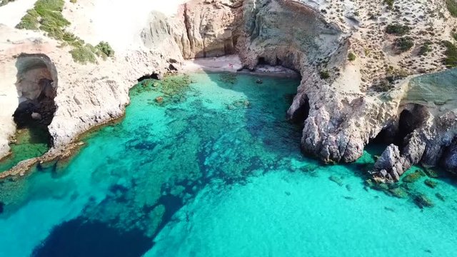 Aerial drone bird's eye view video of iconic volcanic white chalk beach and caves of Tsigrado with turquoise and sapphire clear waters, Milos island, Cyclades, Greece