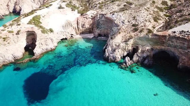 Aerial drone bird's eye view video of iconic volcanic white chalk beach and caves of Tsigrado with turquoise and sapphire clear waters, Milos island, Cyclades, Greece