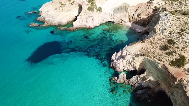 Aerial drone bird's eye view video of iconic volcanic white chalk beach and caves of Tsigrado with turquoise and sapphire clear waters, Milos island, Cyclades, Greece
