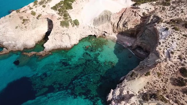 Aerial drone bird's eye view video of iconic volcanic white chalk beach and caves of Tsigrado with turquoise and sapphire clear waters, Milos island, Cyclades, Greece