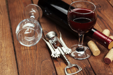 Red wine bottle, wine glass and corkscrew on wooden table background