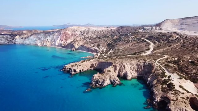 Aerial drone bird's eye view video of iconic volcanic white chalk beach and caves of Tsigrado with turquoise and sapphire clear waters, Milos island, Cyclades, Greece