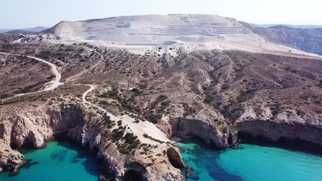 Aerial drone bird's eye view video of iconic volcanic white chalk beach and caves of Tsigrado with turquoise and sapphire clear waters, Milos island, Cyclades, Greece