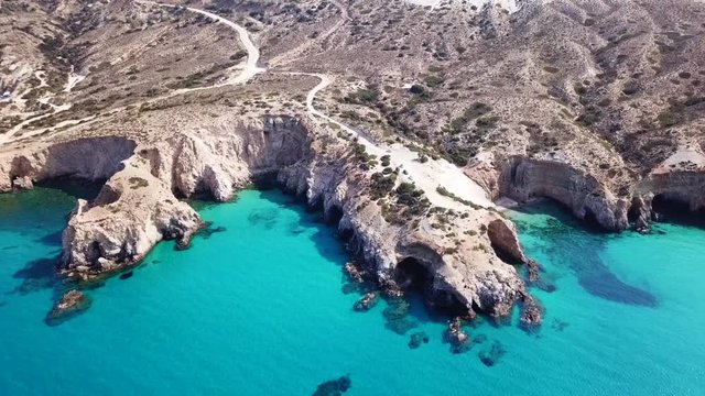 Aerial drone bird's eye view video of iconic volcanic white chalk beach and caves of Tsigrado with turquoise and sapphire clear waters, Milos island, Cyclades, Greece
