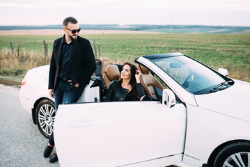 A typical couple of men and women spend time outside the city next to a white car