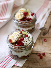 Granola with yogurt and fruit in glass jars on a wooden table. Rustic style.
