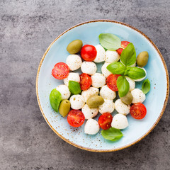 Delicious caprese salad with ripe cherry tomatoes and mini mozzarella cheese balls with fresh basil leaves.