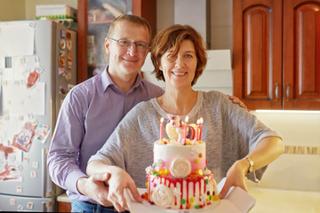 Husband and wife are holding a cake with candles to congratulate their baby.