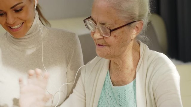 Tilt down of elderly woman and adult granddaughter smiling, waving and talking at camera while web conferencing with family members on digital tablet 