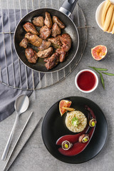 top view of rice, broccoli, fig with sauce on black plate and fried meat in frying pan