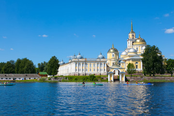 Fototapeta na wymiar SELIGER, RUSSIA. Nilov Monastery on Seliger lake. Yellow building. Blue sky and blue lake in summer. Kayak people in the foreground