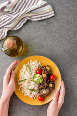 partial view of woman holding plate with rice, meat and broccoli oil