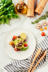 salad on white plate with bottle of oil, cherry tomatoes, lime and rosemary