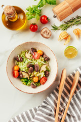 top view of salad on white bowl with bottle of oil, cherry tomatoes, lime and rosemary