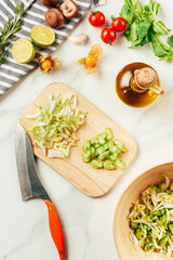 top view of cabbage and celery on cutting board with bottle of oil, cherry tomatoes, limes and rosemary