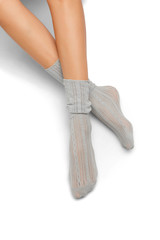 Pair of light-gray lace loose socks on woman’s crossed legs, isolated against the solid color background. Elegant footwear with stylish ornament. Glamorous legwear for fashionable ladies and girls.