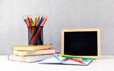 colorful pencils with books and chalkboard on a desk with gray background