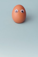 А one brown egg with toy’s eyes on blue background. Easter egg