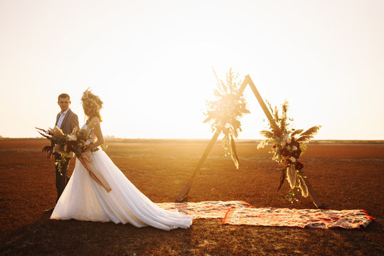 young and beautiful bride and groom enjoy each other. Wedding day in boho style. Sunshine portrait of happy bride and groom outdoor in nature at sunset. Warm summertime.