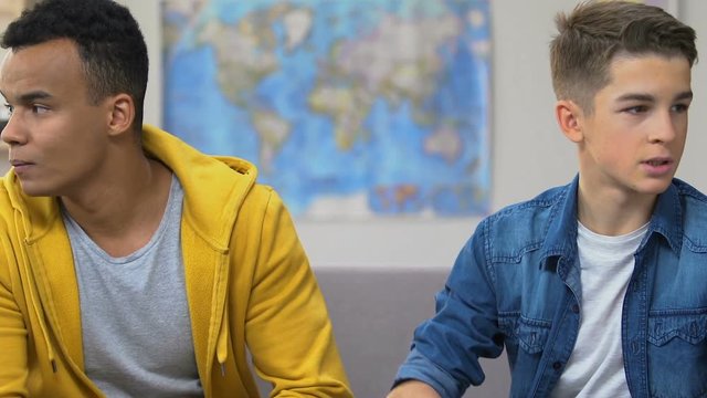 Two teenage boys arguing, sitting on couch, high school relationship problems