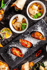 European cuisine. appetizer for wine on a black background. Pate, mini salad, canape, sea products, salmon and mussels in tomato sauce. Top view, copy space