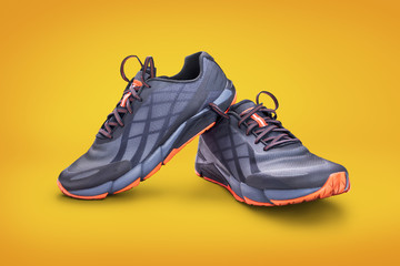 Front view of gray and orange trainers isolated on a yellow background.