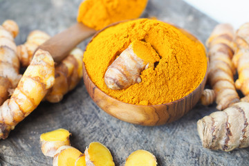 Turmeric powder and fresh turemric in wood bowls on wooden table. Herbs