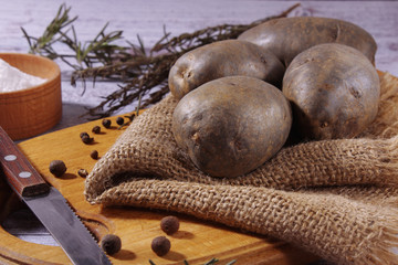 Fresh organic, purple potatoes are lying on a napkin, on a cutting board. Cooking delicious homemade food with aromatic spices and salt