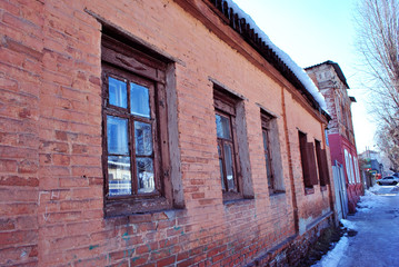 Fototapeta na wymiar Old red brick building wall with windows close up, small town winter street, snow on roof and poplar tree without leaves, bright blue sky