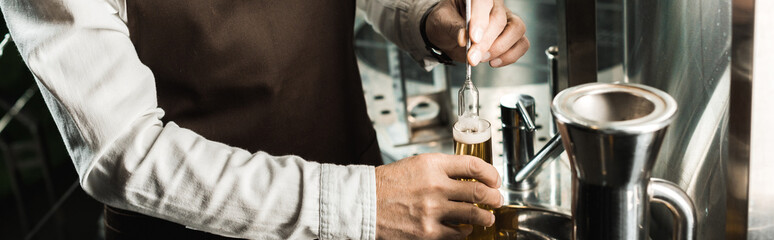 cropped view of brewer examining beer in flask in brewery