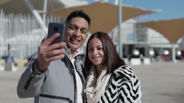 Smiling young couple posing for selfie. Happy people in love taking selfie with smartphone outdoor during sunny day. Relationship concept