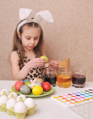 Cute little girl painting easter eggs at home.