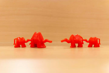 Red toy camels standing in two rows per two against each other. Smaller camels are holding tails of...