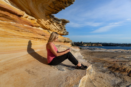 Woman Sitting Under Sandstone Rock Ledge By The Ocean