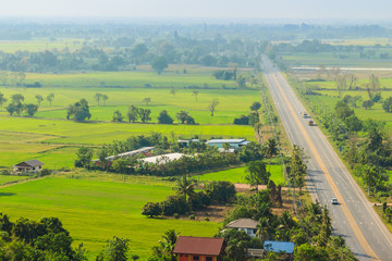 Aerial view over highway from hilltop around with countryside green rice fields and blue sky background. The provincial highway with cars and trucks crossing the hills at Phichit province, Thailand.