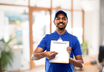 mail service and shipment concept - happy indian delivery man with clipboard in blue uniform over office background