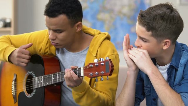 Two teenagers playing guitar and harmonica, musical hobby, amateur musicians