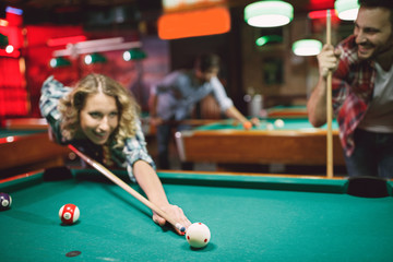 couple have funny time in billiard bar- woman playing snooker.