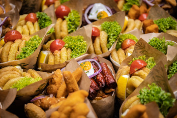 Crowded street fast food. Delicious snack cone with squid sausage quail egg rings of onion salad and tomato in city market for tourists.