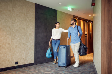 Man and woman arriving at hotel lobby with suitcase at vacation. - obrazy, fototapety, plakaty