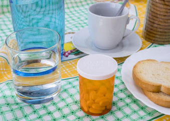 Medication during breakfast, capsules next to a glass of water, conceptual image, horizontal composition