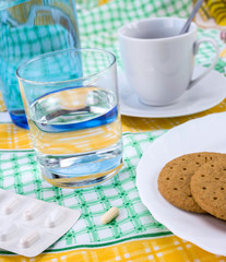 Medication during breakfast, capsules next to a glass of water, conceptual image, horizontal composition