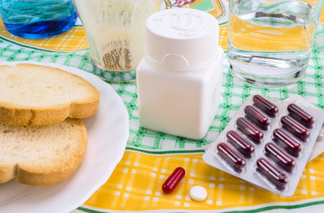 Medication during breakfast, capsules next to a glass of water, conceptual image, horizontal composition