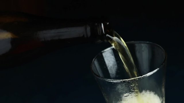 Pouring craft beer from the bottle into drinking glass on dark background close up. Sllow motion full hd video